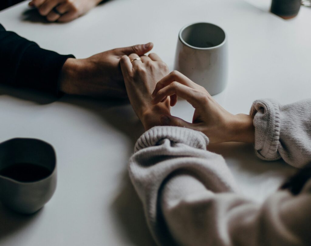 A couple reaches across the table to hold hands, making amends after working through emotional flooding.