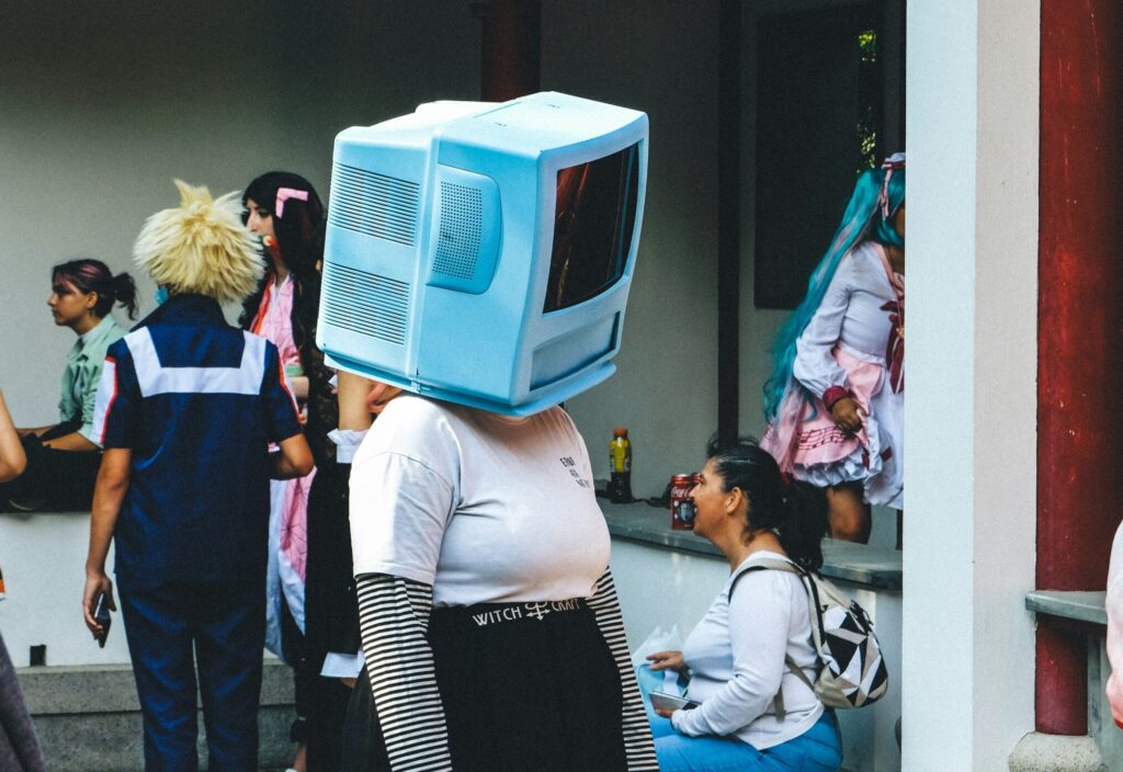A person wearing an old computer monitor as a helmet at a social gathering, representing how artificial intelligence struggles to understand human emotion, connection, and the subtle art of “reading the room.”