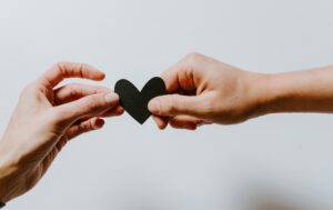 Two hands gently hold a black paper heart, symbolizing love, connection, and emotional attachment.