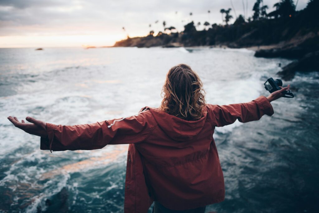 Person standing at the edge of the ocean with arms outstretched, symbolizing emotional release, peace, and freedom after working through anger.